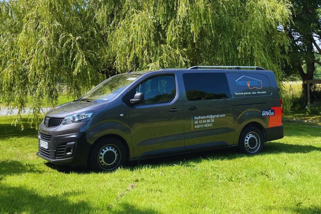 Véhicule professionnel Fredhelec stationné sur un terrain herbeux, logo et coordonnées visibles