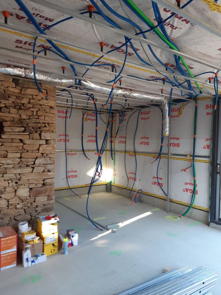 Installation électrique en cours dans une maison en rénovation, câblage et gaines apparentes au plafond.